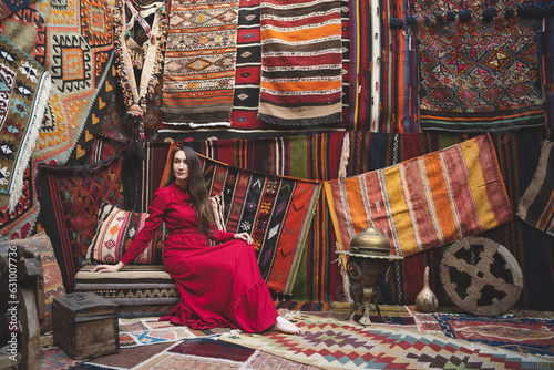 a beautiful girl in a red dress in a traditional turkish interior with many carpets on the wall