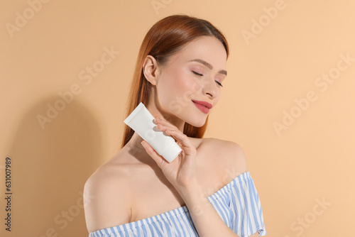 Beautiful young woman holding sun protection cream on beige background