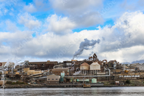 An industrial facility with steam billowing out from pipes, a cloudy blue sky on the Derwent River in Tasmania