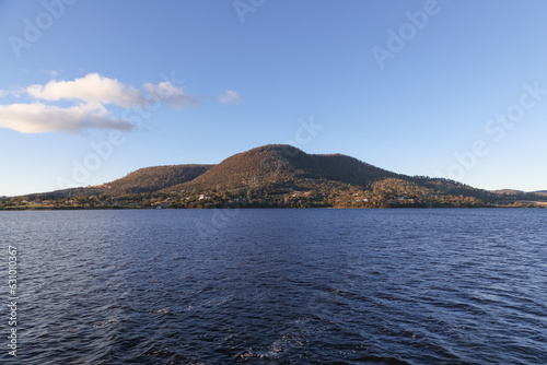 A beautiful landscape of a mountain and a large river with a blue cloudy sky on the Derwent River in Tasmania