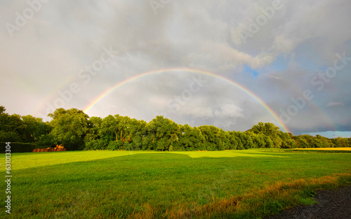 complete rainbow over fields and trees against storm clouds 