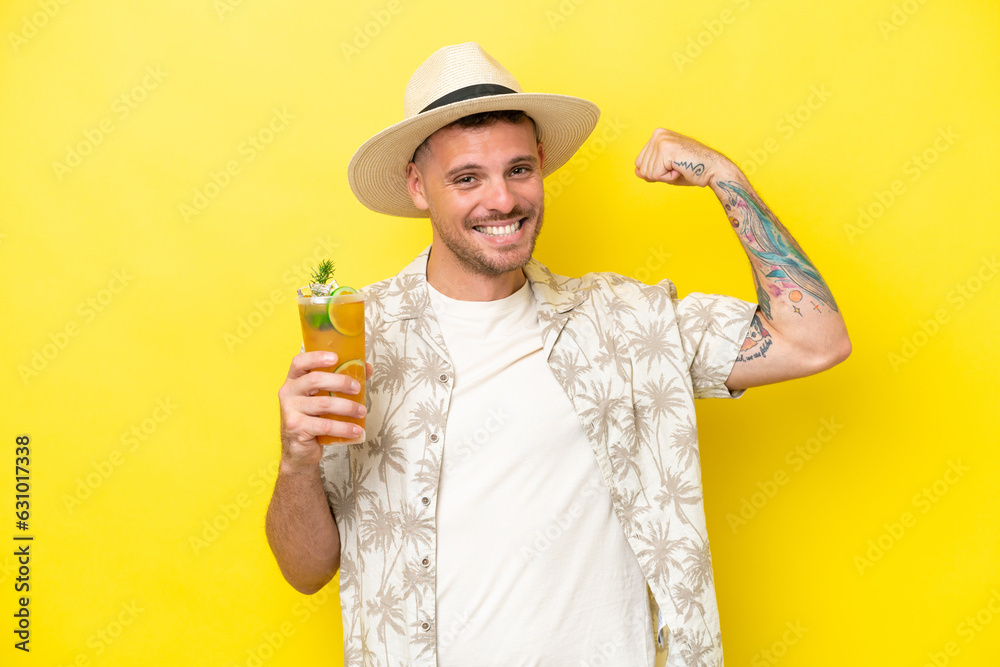 Young caucasian man holding a cocktail isolated on yellow background doing strong gesture Young caucasian man holding a cocktail isolated on yellow background doing strong gesture