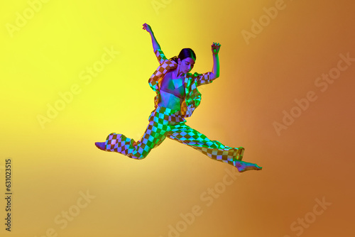 Young woman, professional contemporary dancer in motion, in stylish clothes over gradient yellow orange background in neon light. Concept of modern dance style, hobby, art, performance, lifestyle, ad