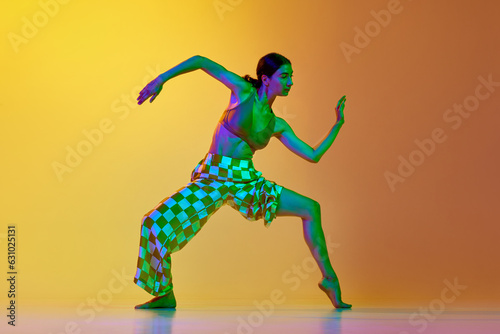 Fototapeta Naklejka Na Ścianę i Meble -  Artistic, dynamic image of young woman in motion, training, dancing against gradient yellow orange background in neon light. Concept of modern dance style, hobby, art, performance, lifestyle, ad
