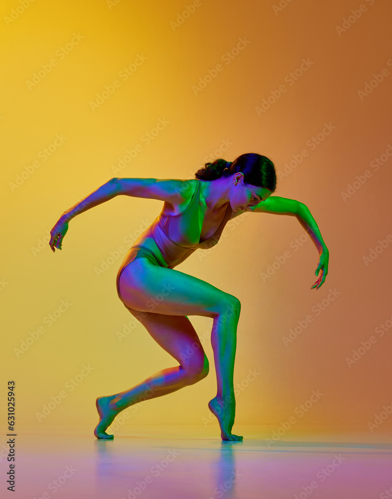 Tender young woman in underwear dancing contemp dance against gradient yellow orange background in neon light. Concept of modern dance style, hobby, art, performance, lifestyle, ad
