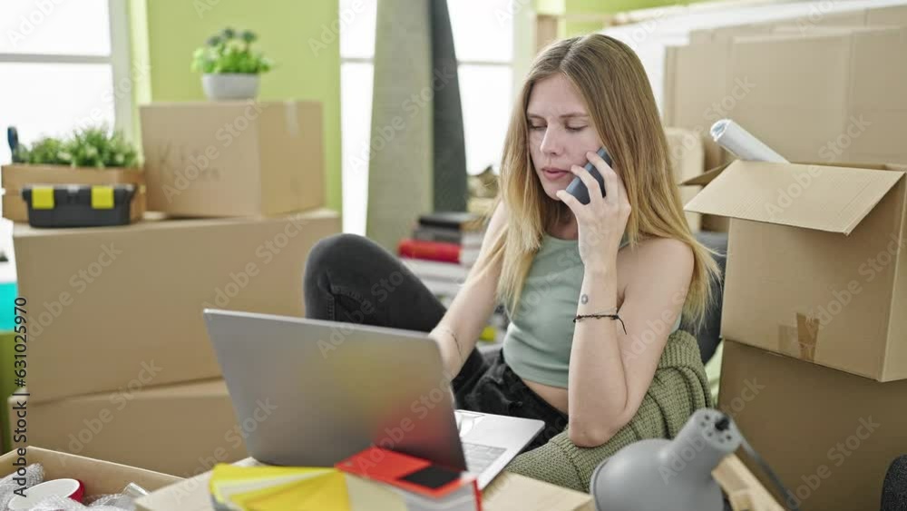 Young blonde woman using laptop talking on smartphone at new home Young blonde woman using laptop talking on smartphone at new home