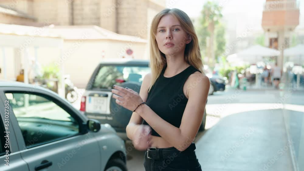 Young blonde woman standing with crossed arms smiling at street Young blonde woman standing with crossed arms smiling at street