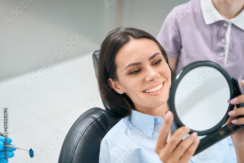 Woman in orthodontic chair looking at mirror, checking quality of teeth whitening