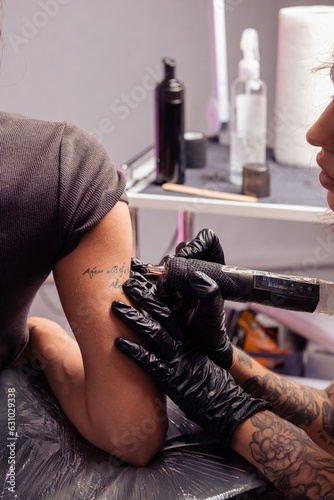 Professional tattoo artist using machine to etch inscription on female arm
