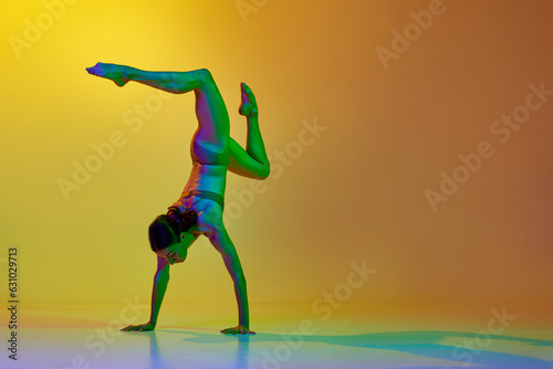 Talented, flexible young woman dancing contemp in underwear against gradient yellow orange background in neon light. Concept of modern dance style, hobby, art, performance, lifestyle, ad
