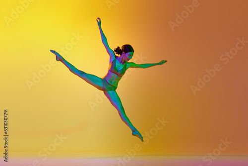 Twine pose. Young talented woman, professional dancer in motion, dancing against gradient yellow orange background in neon light. Concept of modern dance style, hobby, art, performance, lifestyle, ad