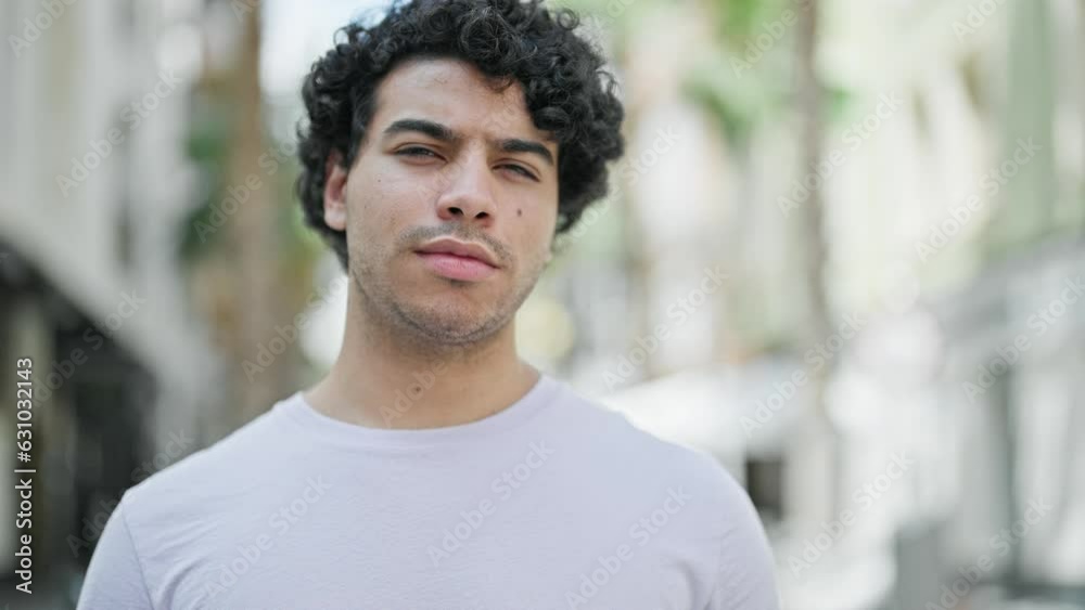 Young latin man standing with serious expression at street