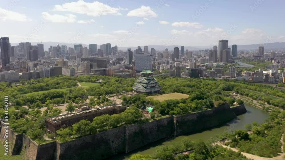 Wide aerial flying towards historic Osaka Castle with park, moat, skyscraper, and city in Osaka, Japan. Wide aerial flying towards historic Osaka Castle with park, moat, skyscraper, and city in Osaka, Japan.