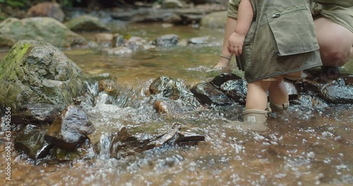 happy family mother holding hand cute little Asian toddler daughter walking in mountain river water creek Learning about Nature in the rainforest, adventure explorer camping travel trip