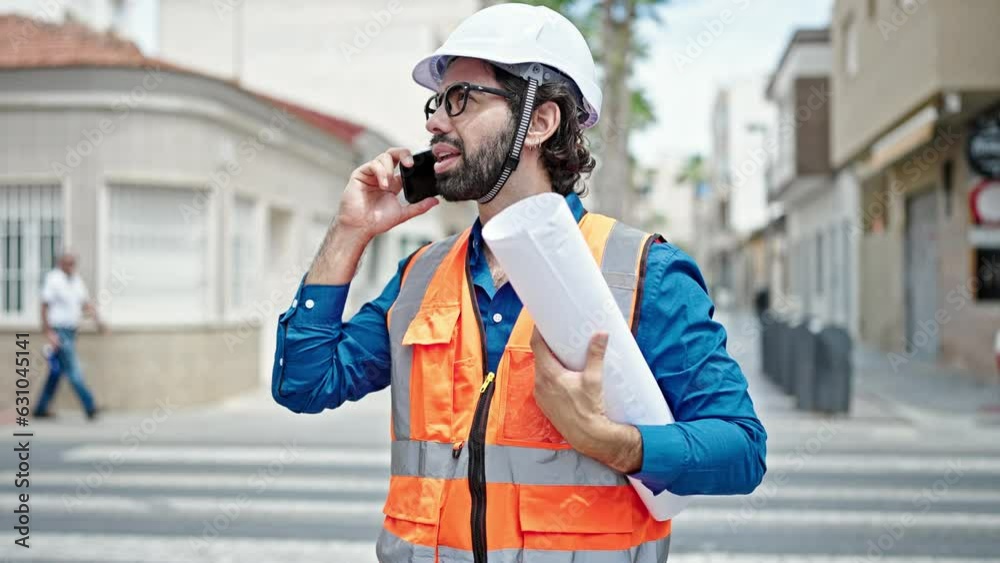 Young hispanic man architect holding blueprints talking on smartphone at construction place Young hispanic man architect holding blueprints talking on smartphone at construction place