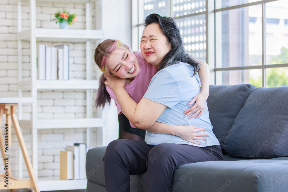 Asian young beautiful daughter standing behind hugging of old senior pensioner retirement cheerful happy healthy fit mother in casual sportswear sitting on sofa couch in living room at home