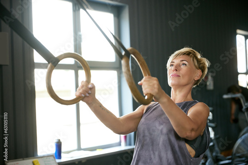 Mature woman training in gym, doing exercises with gymnastics rings. Hand pull-ups exercises. Strength. Concept of active, sportive and healthy lifestyle, fitness, body care, ad