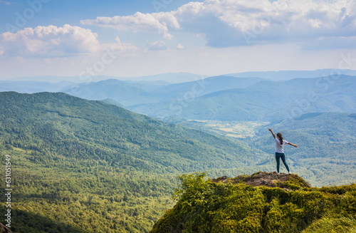 The girl stands on a precipice on a rock and looks at the mountains.Beautiful green mountains in summer with forests, rocks and grass. Water-making ridge in the Carpathians, Carpathian mountains