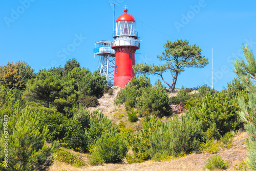 Red Lighthouse on the Frisian island Vlieland, on top of a sand dune with green shrubs and pine trees overlooking the North Sea and the Wadden Sea on a bright summer day, blue sky. High quality photo photo