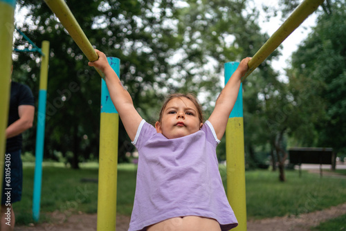 Father with child girl doing pull-ups on workout outdoor area. Healthy active lifestyle, happy family time. Modern fatherhood concept  © troyanphoto