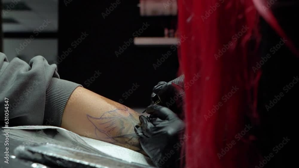 girl tattoo artist with red hair makes a tattoo on the arm in a salon with dark light girl tattoo artist with red hair makes a tattoo on the arm in a salon with dark light