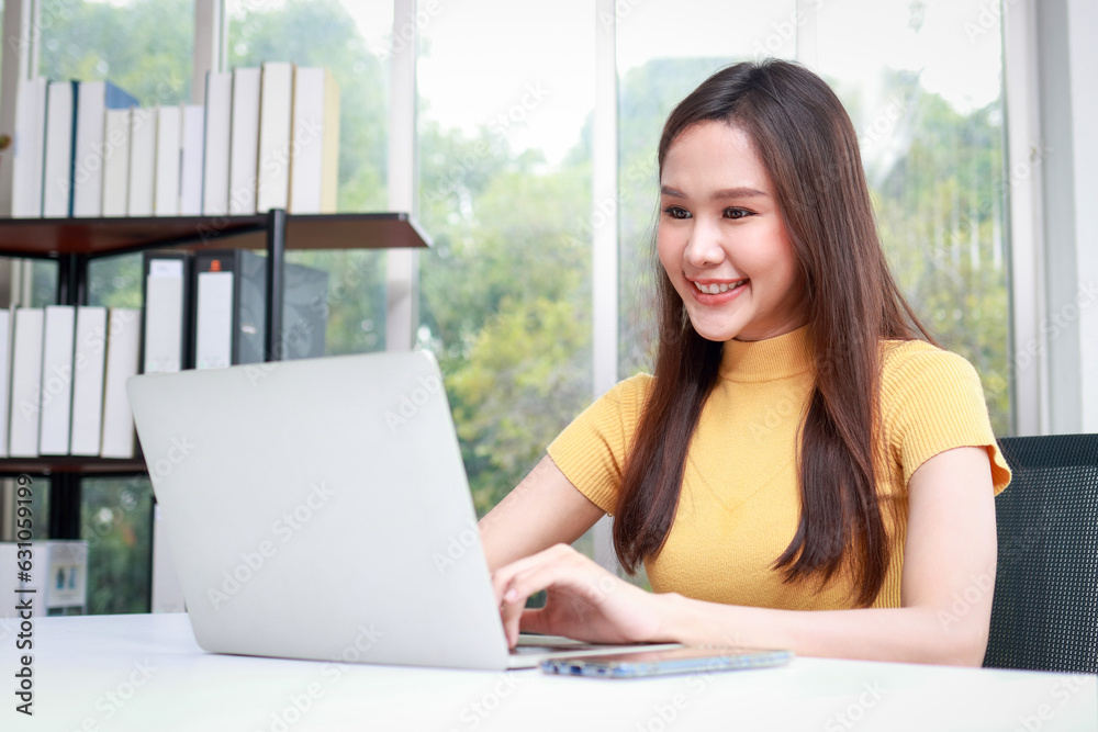Beautiful smiling Asian female worker sitting in the office using a laptop computer to work. business people concept Beautiful smiling Asian female worker sitting in the office using a laptop computer to work. business people concept