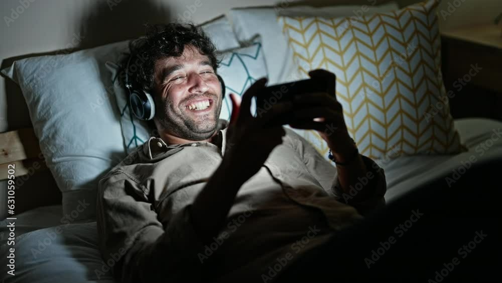 Young hispanic man watching video on smartphone lying on bed at bedroom Young hispanic man watching video on smartphone lying on bed at bedroom