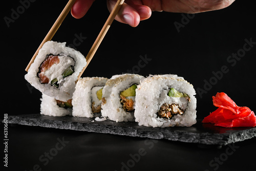 a man eats chopsticks hosomaki rolls with salmon and butter cream and black sesame seeds on a black background