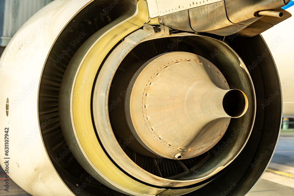 Close up of rear exhaust of a jet engine with yellow glow and spinner, sensor and fan blades visible inside of the cowling.