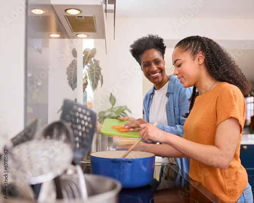 Mother With Teenage Daughter Helping To Prepare Meal At Home In Kitchen Together