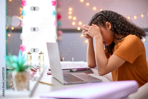 Stressed Teenage Girl At Home In Bedroom Being Bullied Online Looking At Laptop Computer