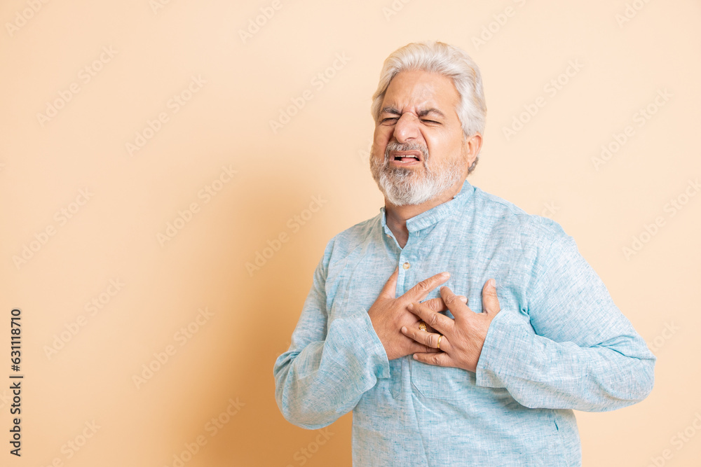 Senior indian man suffering from chest pain, heart attach, isolated on beige background., Fitness and health care, emergency symptoms, Aging, Copy space. Senior indian man suffering from chest pain, heart attach, isolated on beige background., Fitness and health care, emergency symptoms, Aging, Copy space.