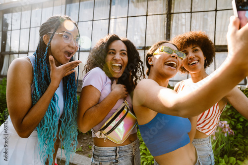 Group of joyful women taking selfie while spending time together outdoors