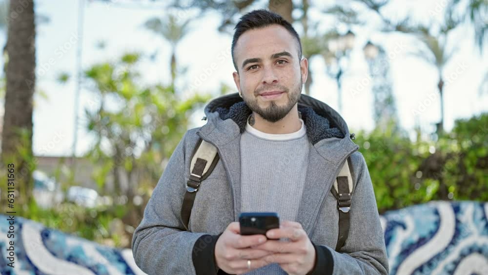 Hispanic man using smartphone smiling at the park Hispanic man using smartphone smiling at the park