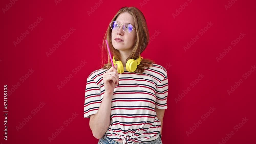 Young blonde woman wearing headphones pointing to camera with doubt expression over isolated red background Young blonde woman wearing headphones pointing to camera with doubt expression over isolated red background