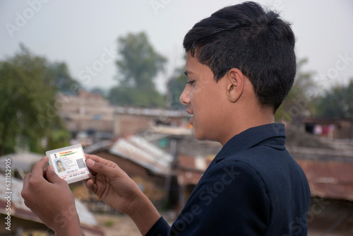 Indian school boy wearing a dark blue school uniform holds his Aadhar card in hand with a smiling face. outdoor background