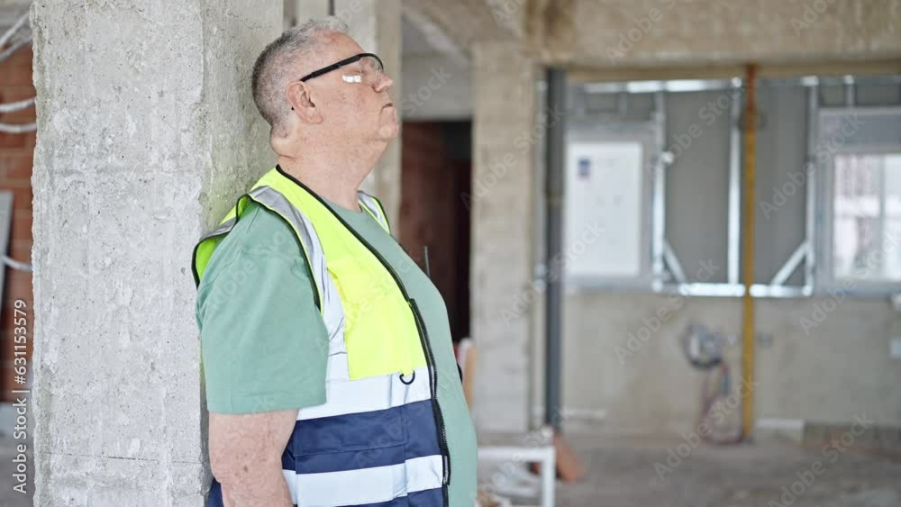 Middle age grey-haired man builder leaning on wall tired at construction site Middle age grey-haired man builder leaning on wall tired at construction site