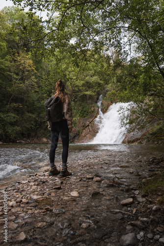Woman standing enjoying the waterfall of the Poza de los Caballos of the Nervion river in Delika, Alava, Basque Country.
