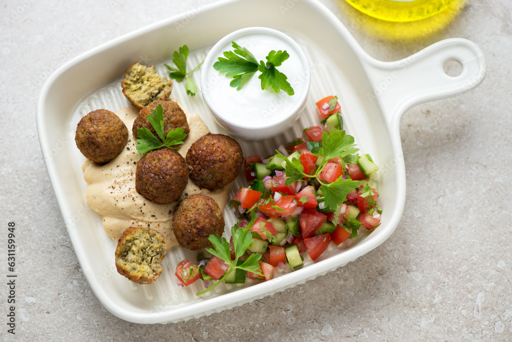 Beige serving tray with falafel, hummus, tomato salsa and yogurt, horizontal shot, elevated view