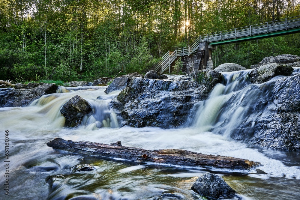 Brook cascading down rocks with a wooden bridge visible in the distance. Brook cascading down rocks with a wooden bridge visible in the distance.