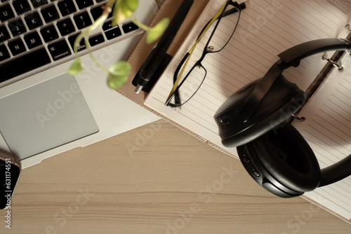 Top view of office Workplace with open laptop, a blank open note book, a smart phone ,a pen, a specs and a head phone on a wooden desk