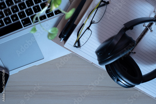 Top view of office Workplace with open laptop, a blank open note book, a smart phone ,a pen, a specs and a head phone on a wooden desk