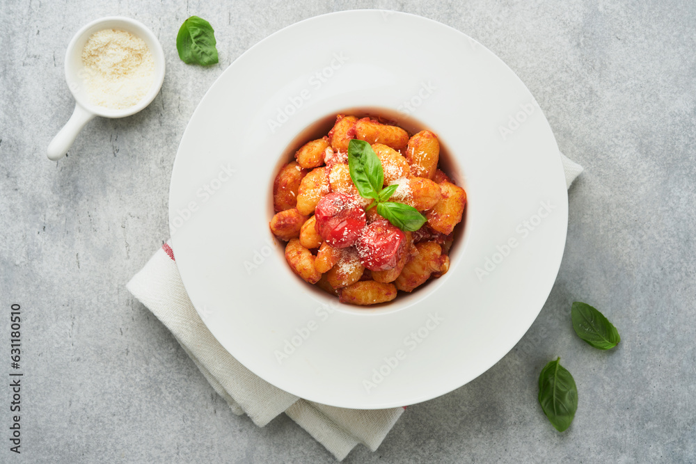 Potato gnocchi. Traditional homemade potato gnocchi with tomato sauce, basil and parmesan cheese on kitchen table on light grey kitchen table background. Traditional Italian food. Top view. Potato gnocchi. Traditional homemade potato gnocchi with tomato sauce, basil and parmesan cheese on kitchen table on light grey kitchen table background. Traditional Italian food. Top view.