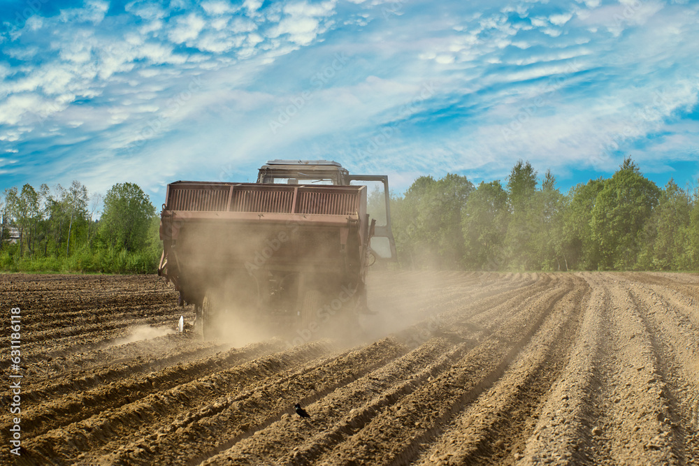 Fototapeta premium Potato planter in agricultural field raises cloud of dust in dry spring during sowing field work.
