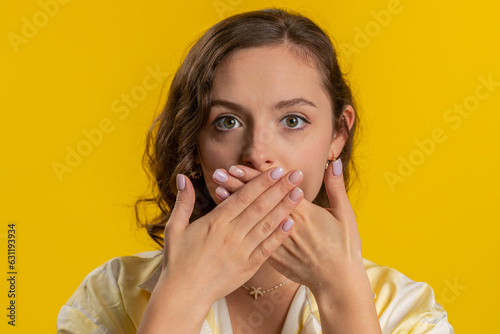 I will not say anything. Frightened woman closing mouth with hands, looking intimidated scared at camera, gestures no, refusing to tell terrible secret, unbelievable truth. Girl on yellow background