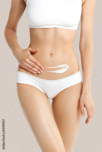 Fototapeta Naklejka Na Ścianę i Meble -  White slim girl in white lingerie applies cream to her lower abdomen
