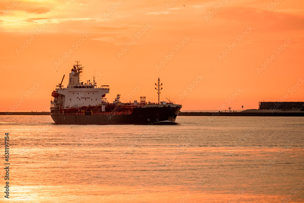 Orange summer sky over an oil tanker going into a port at sunset