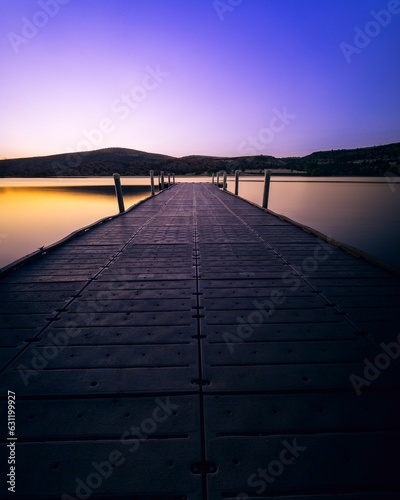 Fototapeta Naklejka Na Ścianę i Meble -  Tranquil pier extending out into a tranquil lake with a breathtaking sunset in the background.