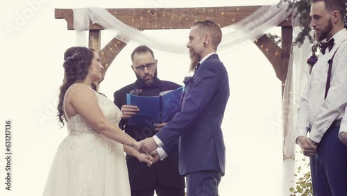 Happy marriage officiant reading wedding vows between a Caucasian grom and a bride outdoors