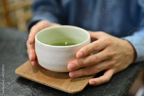 Close up and cropped image of man's hands holding tea cup , Japanese traditional matcha tea, Genmaicha Uji latte in the Japanese tradition ceramic bowl.
